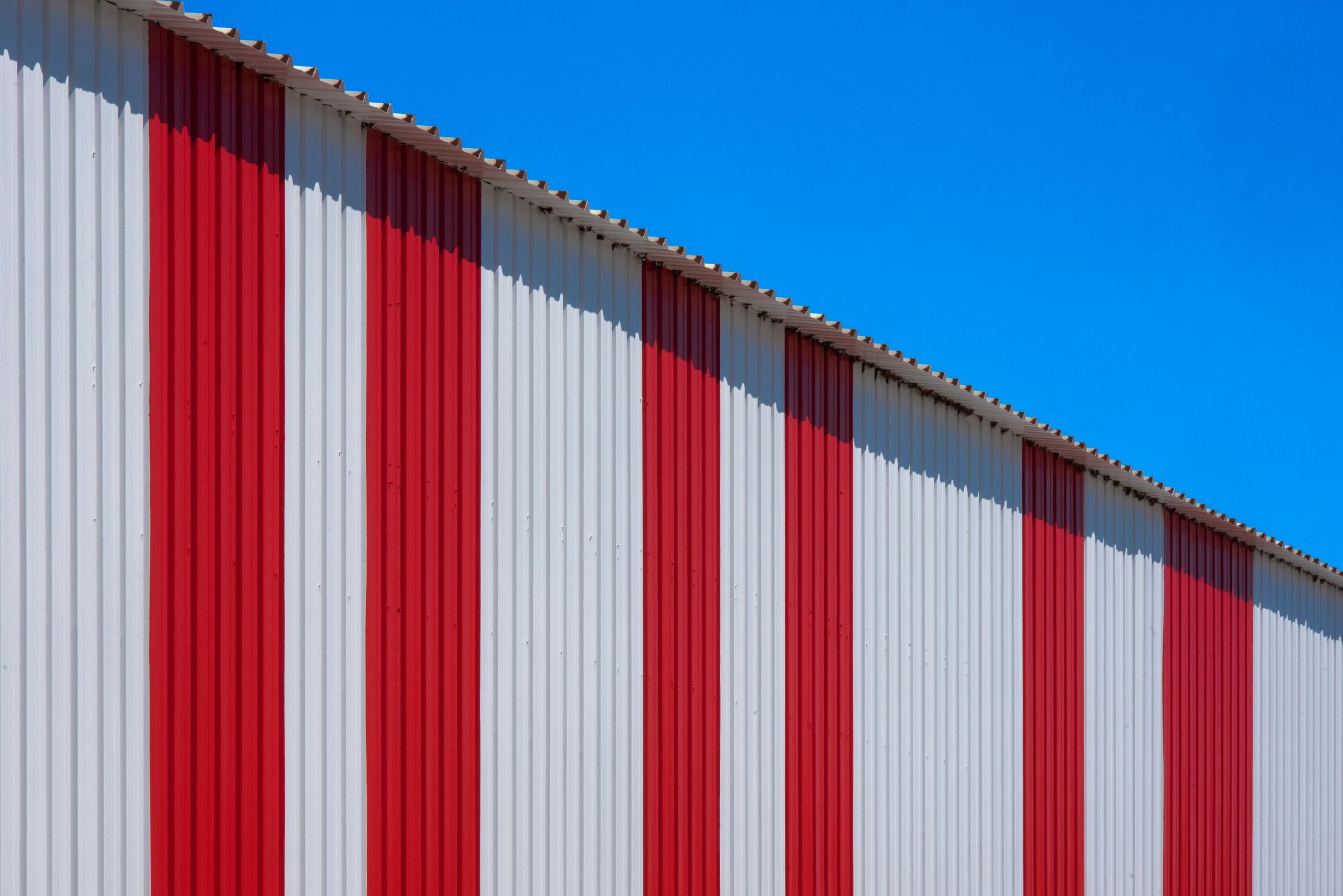 Bâtiment industriel en bardage métallique rayé rouge et blanc sous un ciel bleu